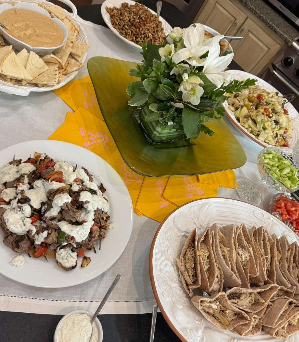 A Mediterranean spread featuring grilled beef with yogurt sauce, pita bread, salads, rice, and a fresh floral centerpiece.
