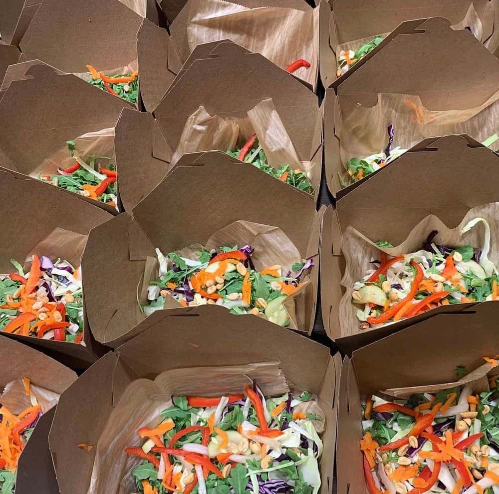 A row of takeout boxes filled with fresh mixed salads, featuring shredded cabbage, carrots, red peppers, and nuts for added crunch.