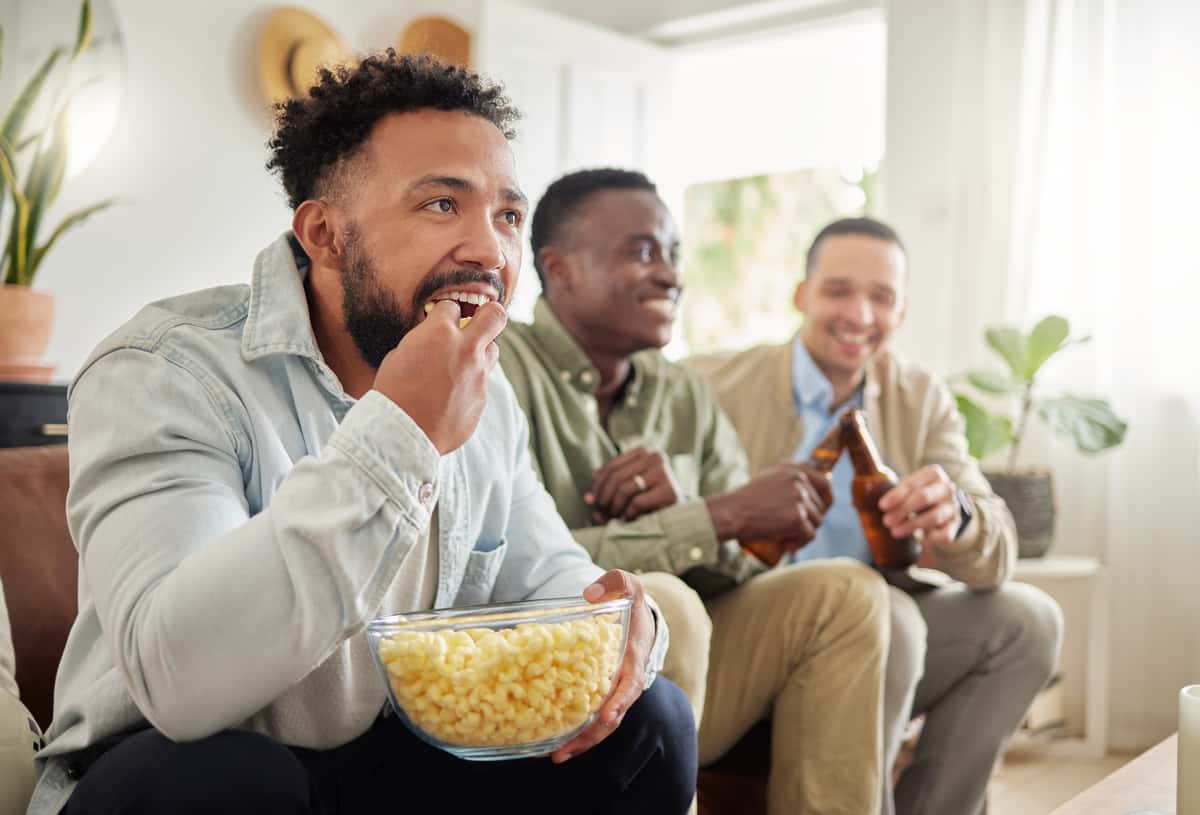3 men watching a sports game, eating and drinking