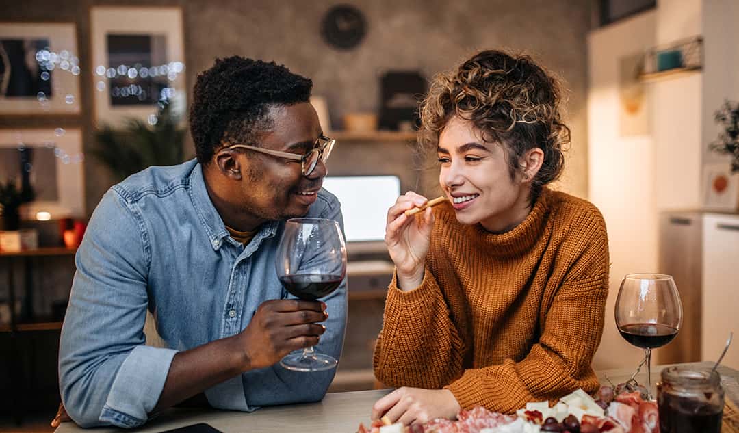 Young interracial couple enjoying charcuterie and sharing wine together on a date night at home
