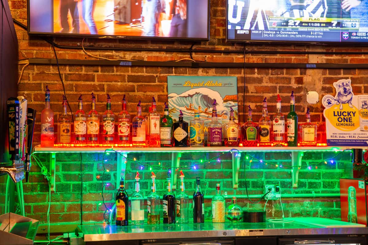 Bar shelves with liquor bottles, neon lighting, and TVs inside The Gaslight Pizza & Grill in Huntingburg, Indiana