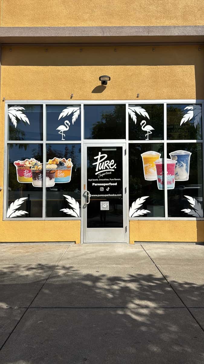 Pure Superfood storefront with window graphics showcasing colorful smoothie bowls and protein-packed drinks against a sunny exterior.