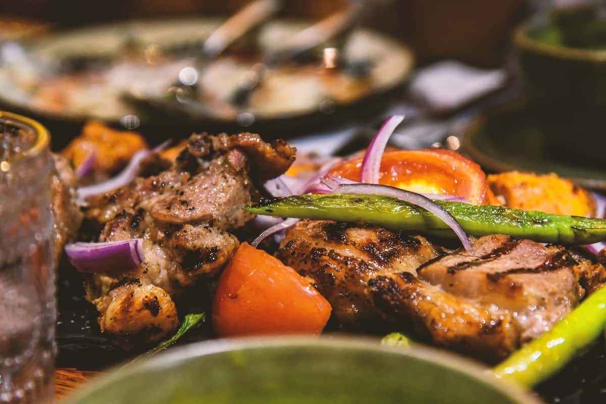 Grilled chicken thighs with charred asparagus, red onion slices, and roasted tomatoes, served on a sizzling hot plate.