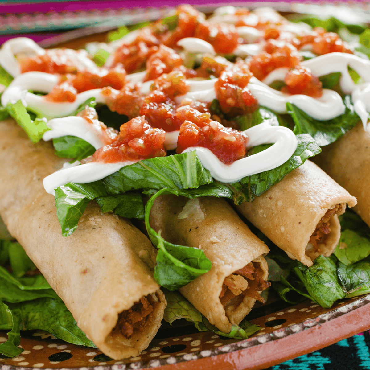Crispy taquitos topped with lettuce, salsa, and drizzled sour cream on a traditional Mexican-style plate.