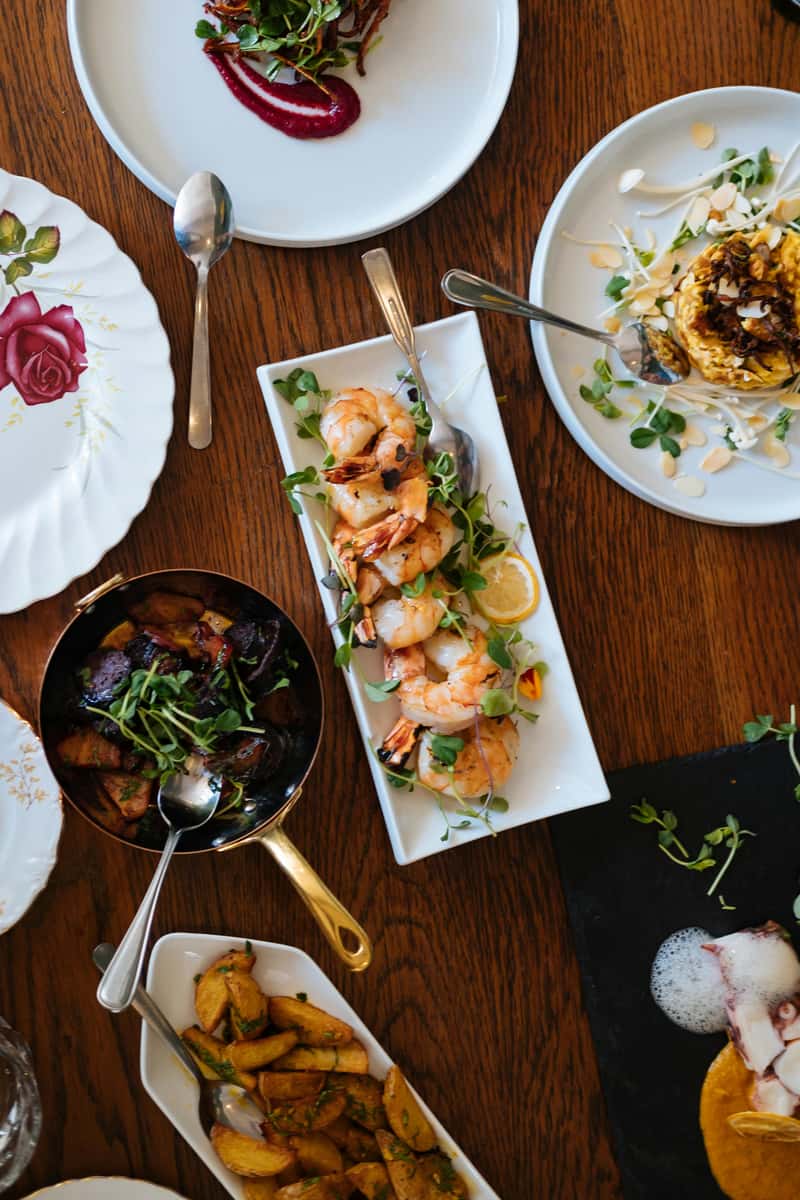 Assorted gourmet dishes on a wooden table, featuring grilled shrimp, roasted vegetables, and creatively plated appetizers.