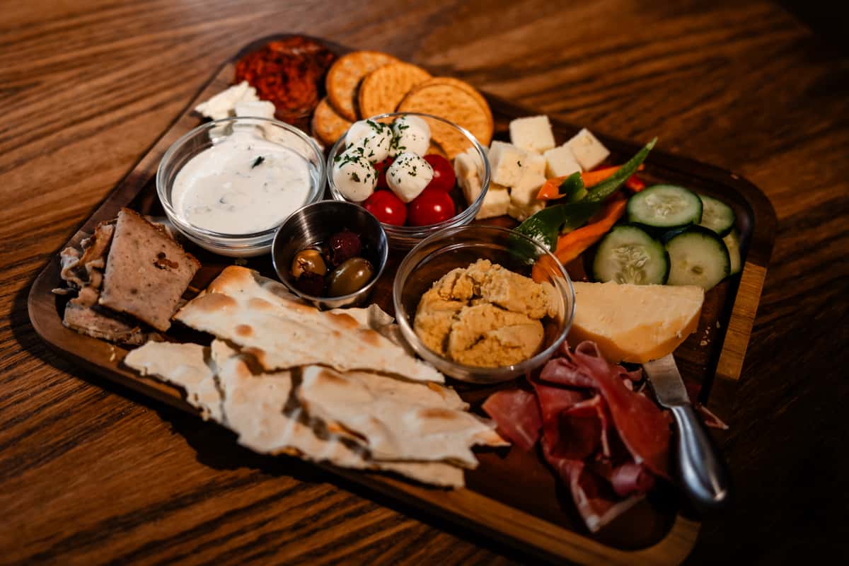 Mediterranean Charcuterie Board 27 Shaved gyro, artisan cured meat, and Mediterranean cheeses served with creamy hummus, Tzatziki, fresh vegetables, olives and lavash for sharing.