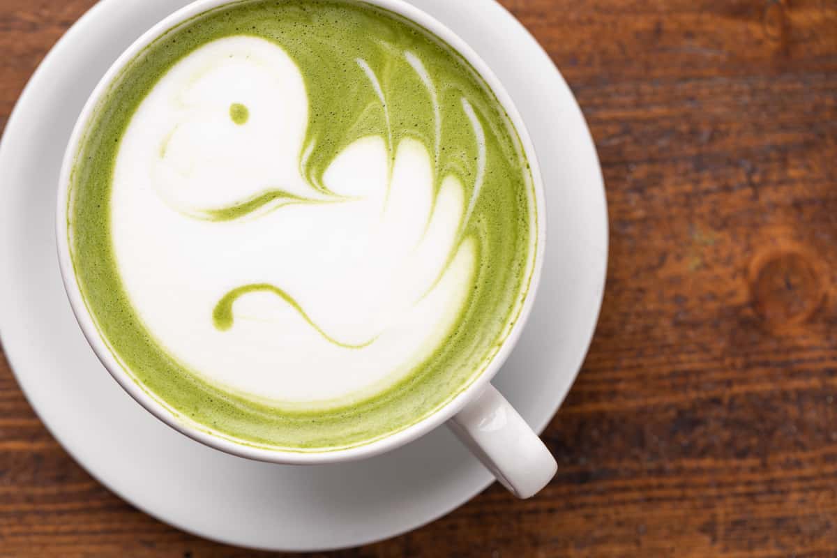 Green Tea Matcha Latte with bird design on a wood background by Coral Tree Cafe