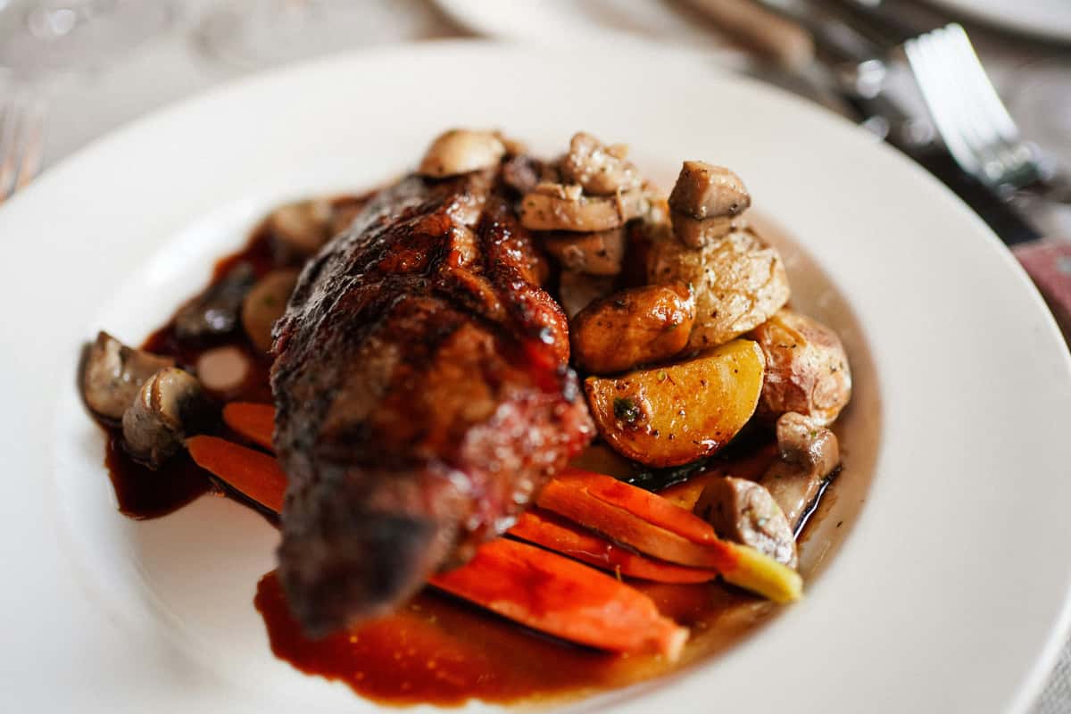 Grilled steak served with roasted potatoes, carrots, mushrooms, and a rich brown sauce on a white plate.