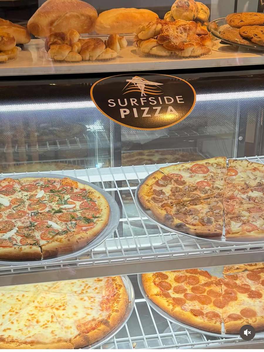 Assorted specialty pizzas on display at Sureside Pizza, including pepperoni, cheese, and veggie options in a glass case, highlighting a local Italian pizzeria with fresh baked goods and a welcoming atmosphere.