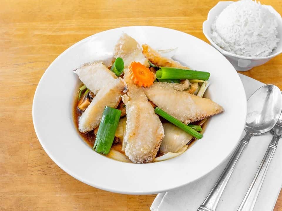 Plate of crispy fried fish fillets with scallions and carrots in a rich soy-based sauce, served with a side of steamed jasmine rice—an elegant Asian-inspired seafood dish.
