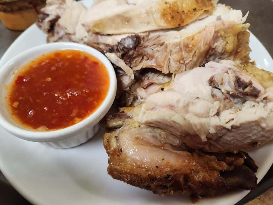 Plate of juicy Thai-style grilled chicken, cut into tender pieces and served with a side of spicy sweet chili dipping sauce—perfect as a flavorful entrée or appetizer in Thai cuisine.