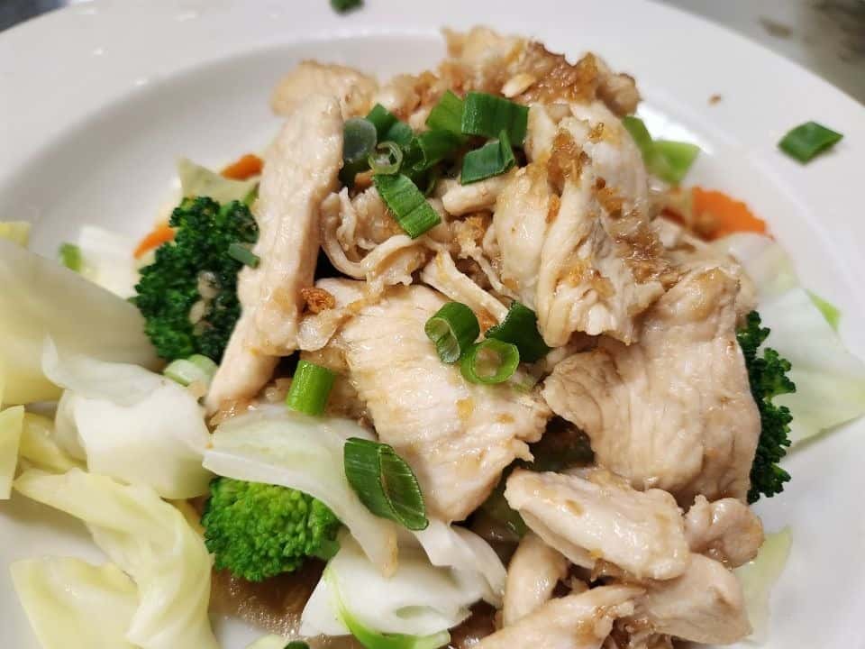 Sautéed chicken breast strips over stir-fried vegetables including broccoli, cabbage, and carrots, garnished with chopped green onions on a white plate.