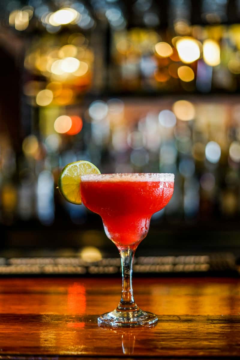 Refreshing red margarita with lime garnish on a salt-rimmed glass at a dimly lit cocktail bar