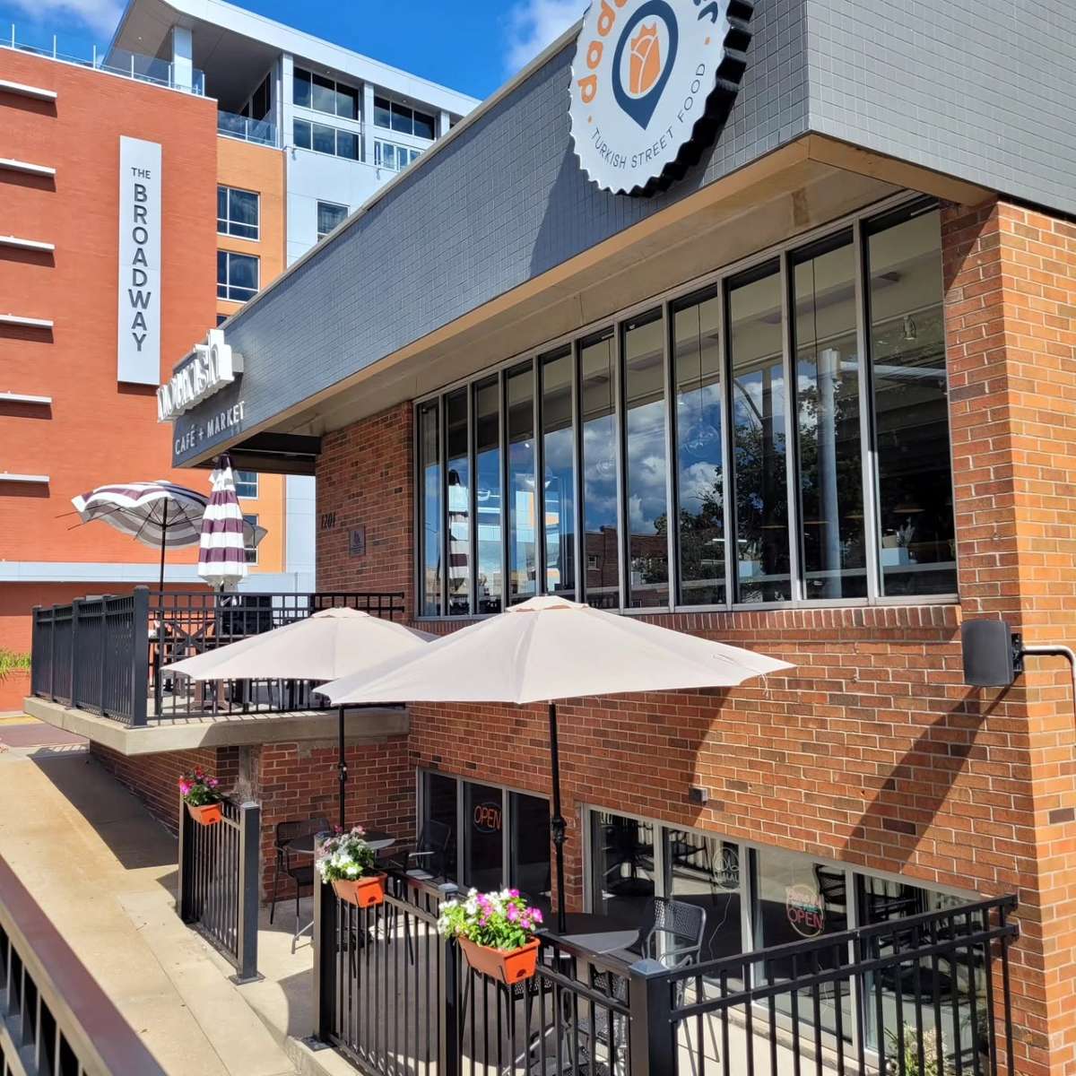Exterior of Dönerish Cafe & Market with brick facade, large windows, and a shaded outdoor seating area.