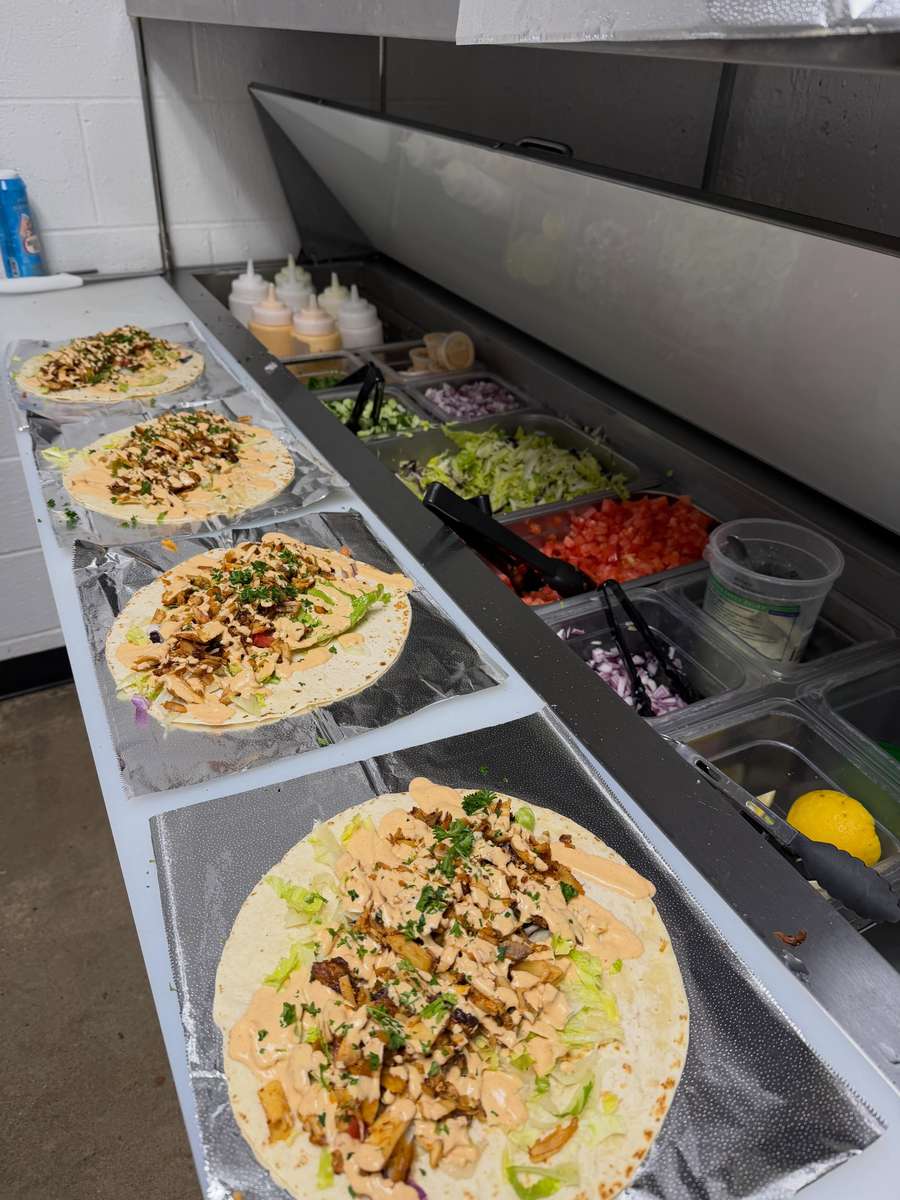 Fresh Turkish wraps being assembled on a restaurant prep line with seasoned döner meat, lettuce, herbs, and creamy house sauce alongside fresh toppings