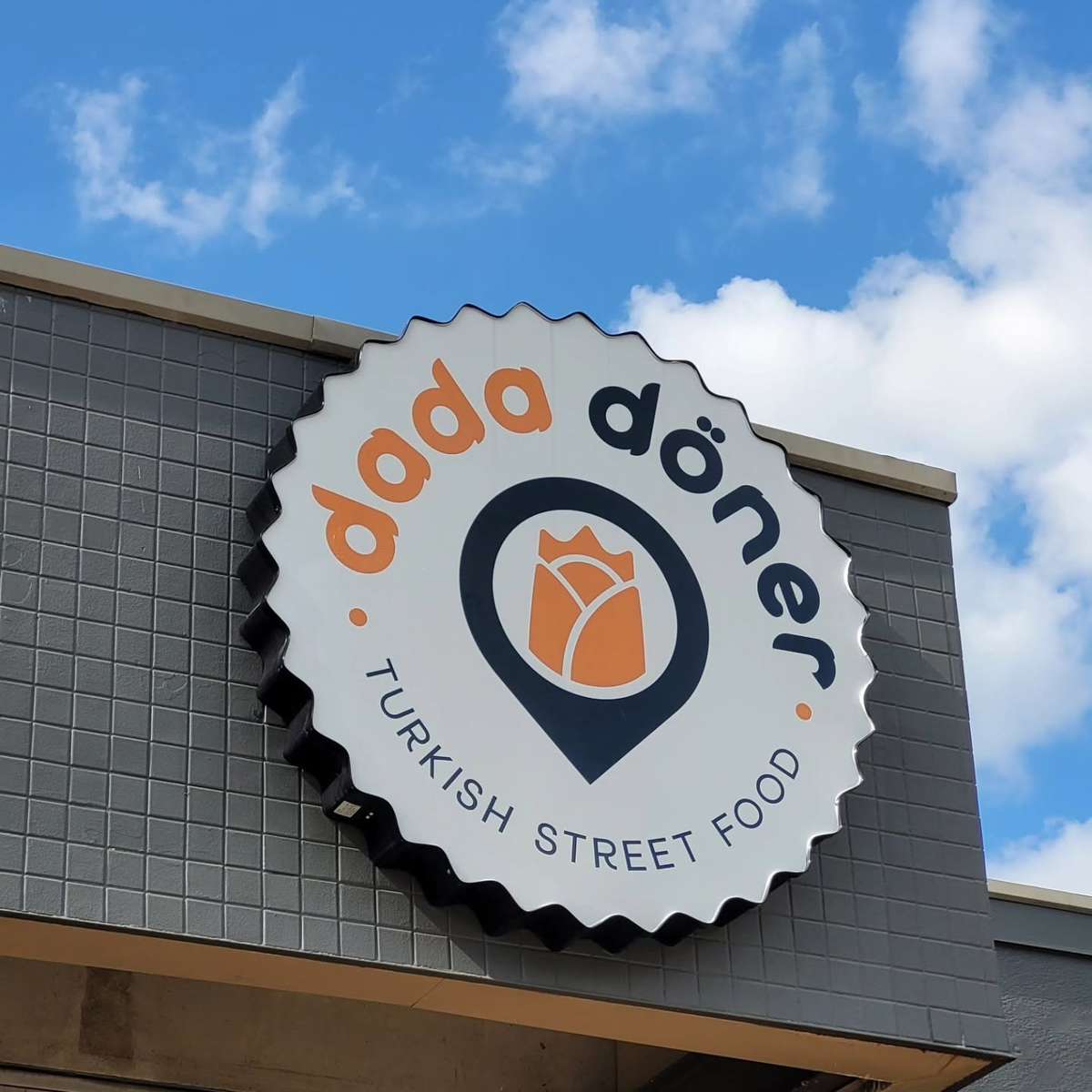 Döner Turkish Street Food storefront sign featuring a modern logo with a tulip icon on a gray tiled exterior under a bright blue sky