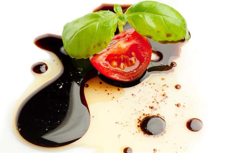 traditional balsamic drizzled on a plate with a small sliced tomato and basil leaf