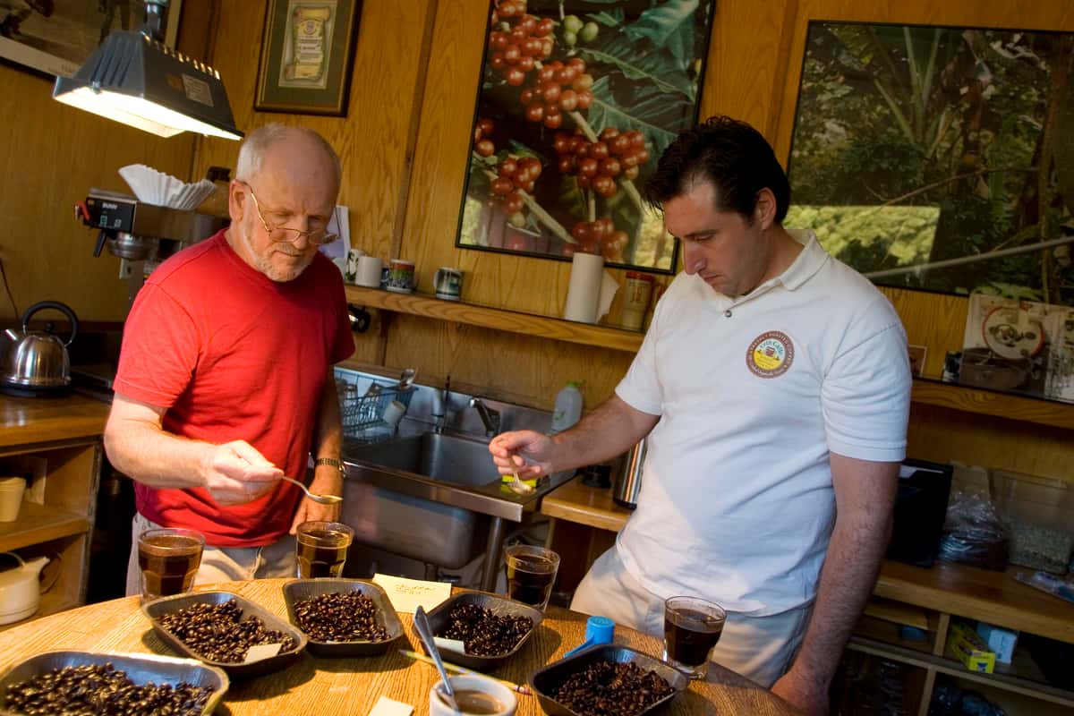 Man in red shirt and man in white shirt sample cups of coffee
