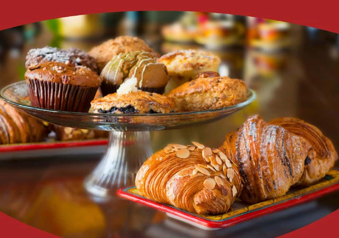 Urth Caffé trio of croissants in the foreground with a variety of pastries such as muffins and scones on a glass pedestal dish behind the croissants.