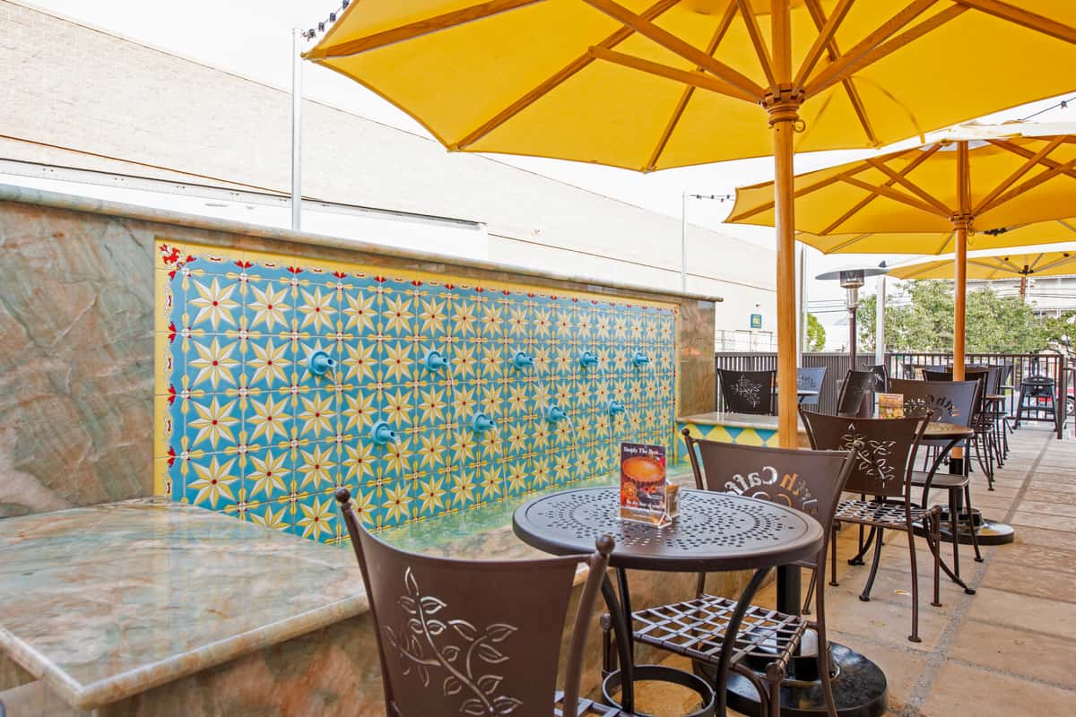 Patio tables with open bright yellow umbrellas and tile fountain