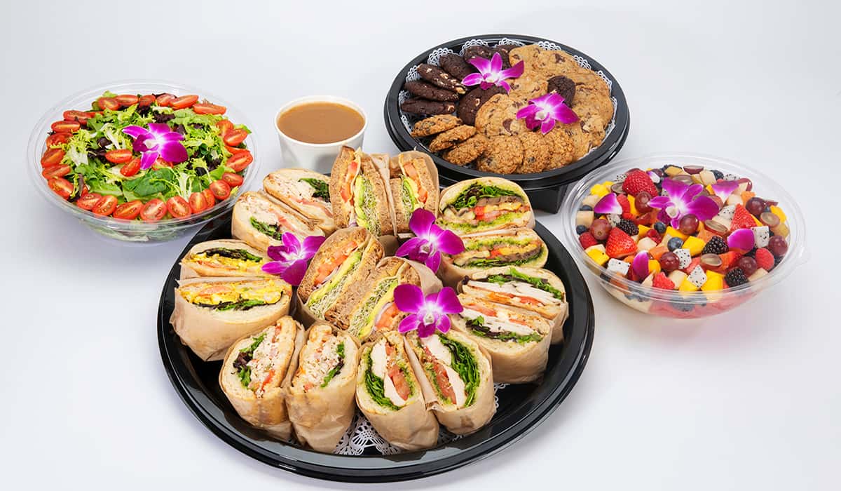 Urth Online Catering Lunch option with round platter of cut in half sandwiches, a bowl of salad with a side of dressing, fruit bowl and plate of cookies
