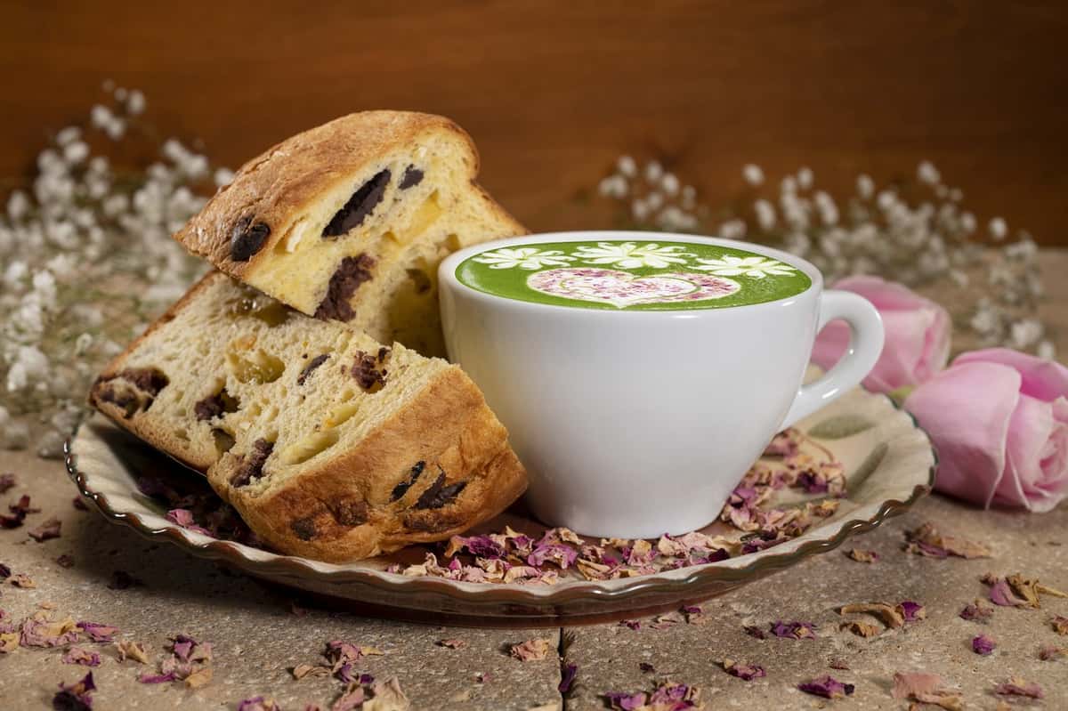Panettone slices with a green rose matcha latte on a saucer with roses and baby' breath flowers in background