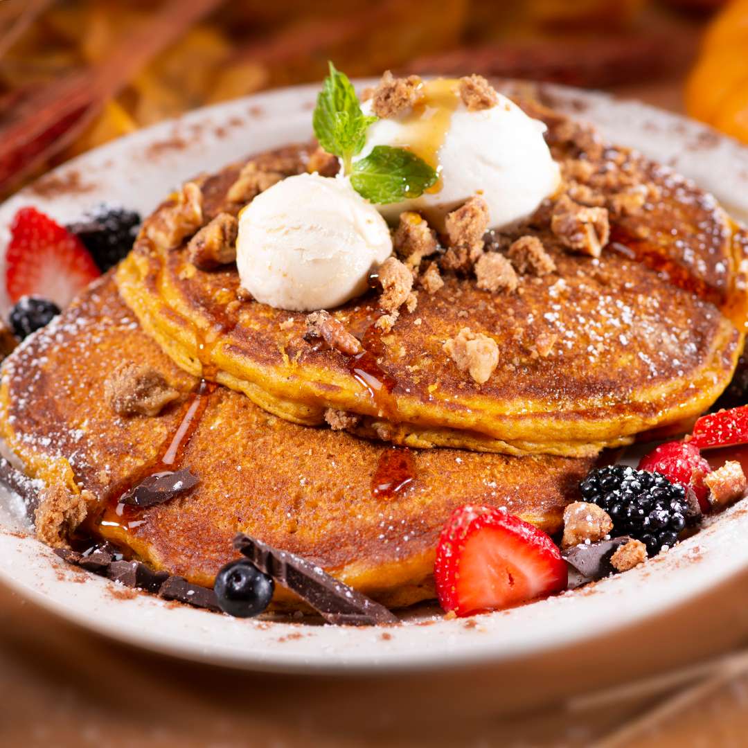 Two Pumpkin Pancakes topped with dollops of whipped cream, Acacia honey butter and pie crust crumbles, garnished with fresh berries