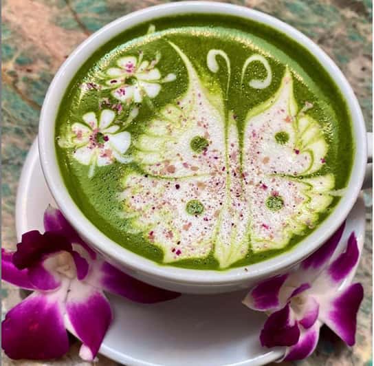 Green Rose Latte with detailed butterfly design made with green tea, oat milk, with rose petal bits sprinkled on top