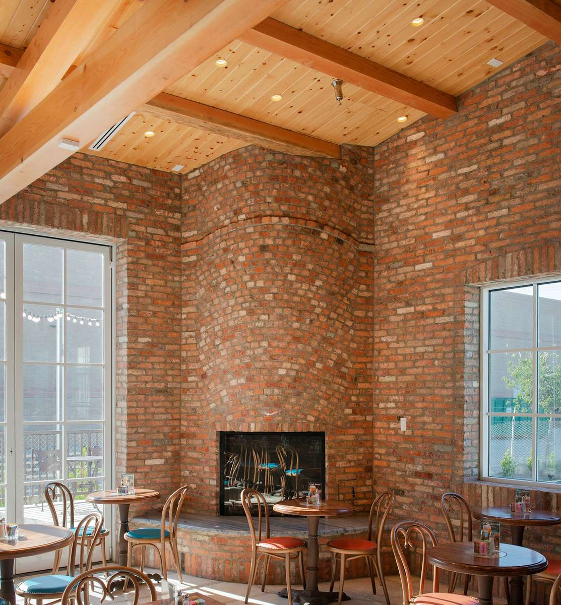 Rounded fireplace of reclaimed brick in corner of room with high ceilings and large windows.