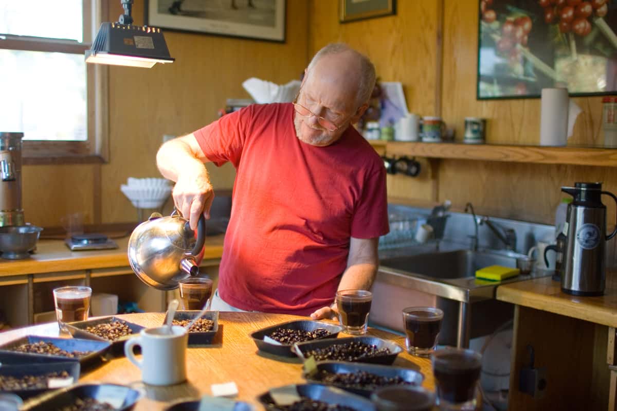 Man in red shirt pours almost boiling water into cups of coffee grounds