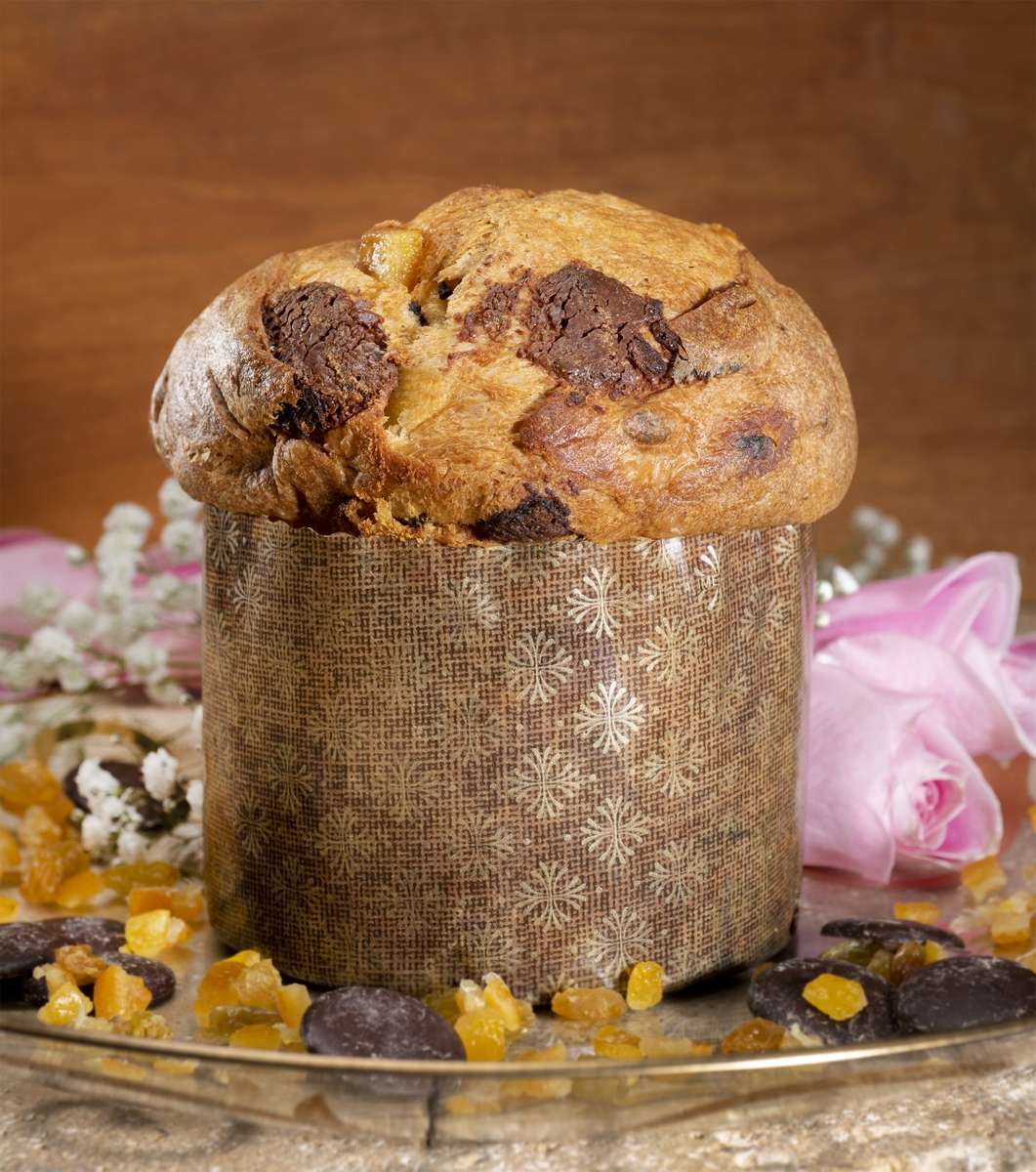 Valentine Panettone with chocolate from Ecuador on a gold-edged platter with bits of orange and chocolate, background with pink roses and white baby's breath.