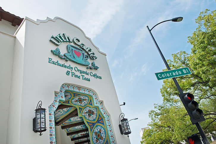 Front facade and entrance to Urth Caffé Pasadena with large logo signage at the top. To the right is a streetlight with a green Colorado Blvd.street sign.