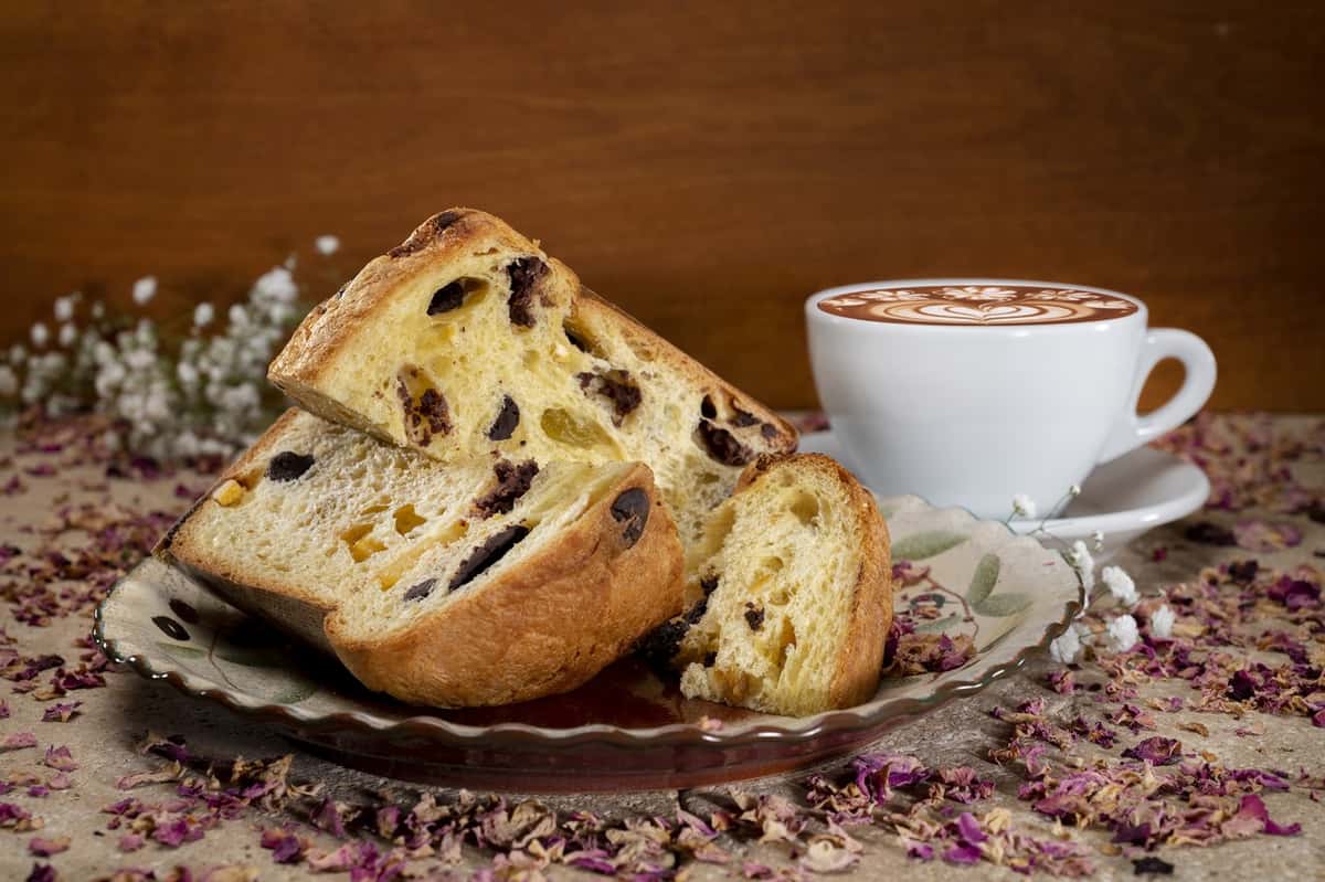 Panettone slice on a saucer with an espresso latte with roses and baby' breath flowers in background