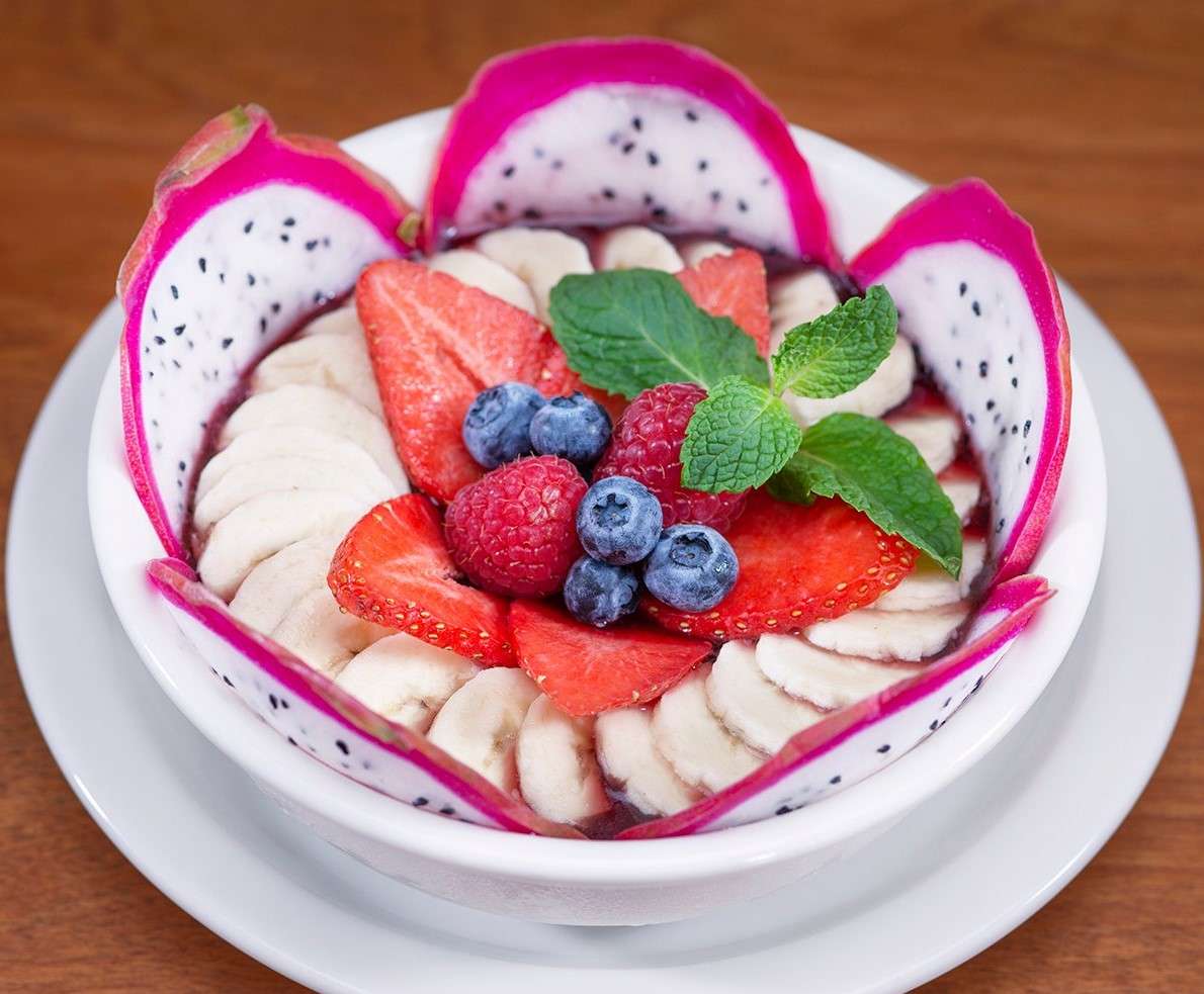 Urth Acai Bowl in white bowl with sliced fruits - acai, bananas, strawberries, garnished with blueberries and raspberries and mint sprig