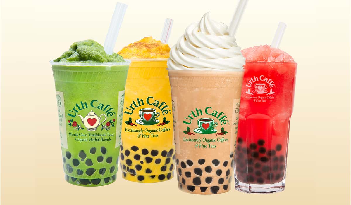 Colors of Urth Drinks -colorful line up of four Urth boba drinks in clear To Go cups with Urth logos including from left to right a blended green tea, a yellow blended Rumi latté, a light brown mocha with swirled whipped cream on top and a light red watermelon smoothie.