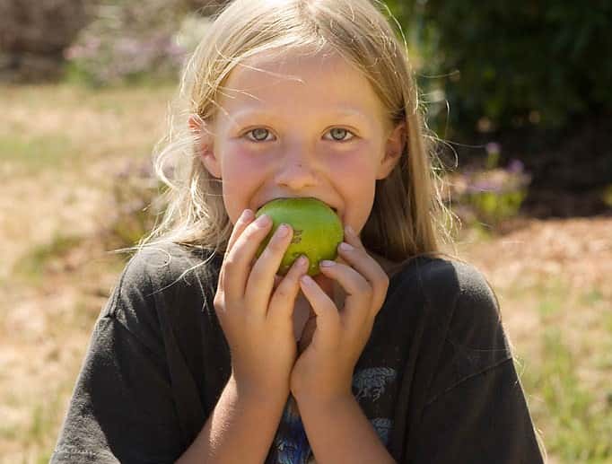 Young girl take a bite out of a green apple