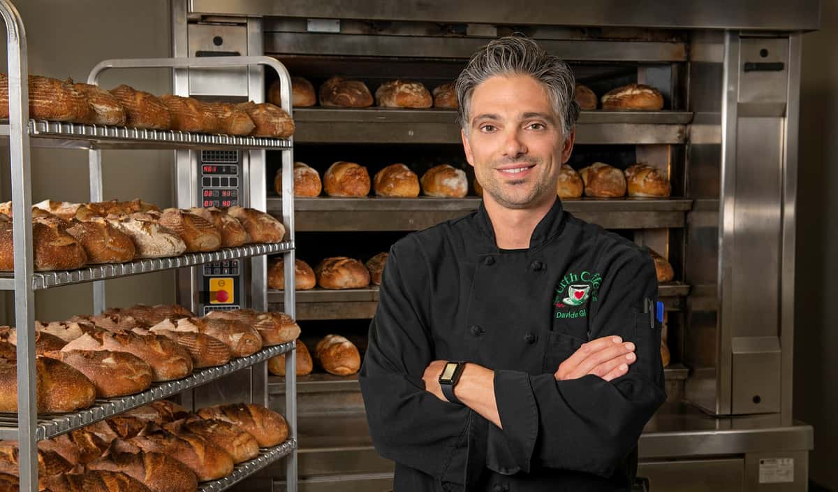 Davide Giova, Urth Caffé Master Baker and Chef, is shown in bakery next to fresh baked breads.