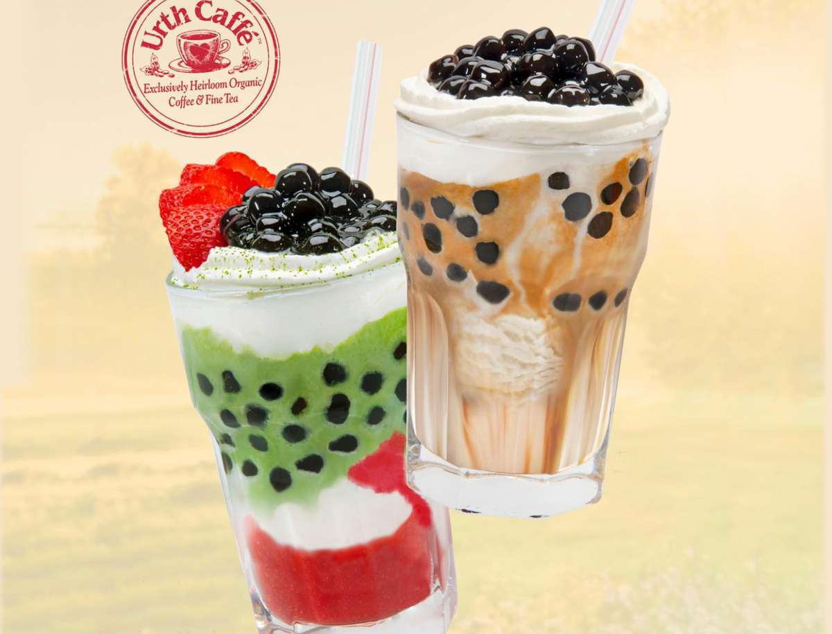 Urth's new Strawberry Matcha Affogato & Espresso Affogatos Bobas with a pile of fresh blueberries on top. The full to the brim glasses are floating slightly tilted outward in front of a light yellow background. There is a round red Urth Caffé stamp logo in the upper left corner.