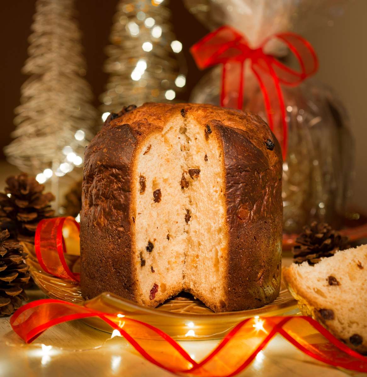 Christmas Panettone with a slice cut out of it to show candied orange and lemon peels and raisins, decorated with red ribbon and a holiday background