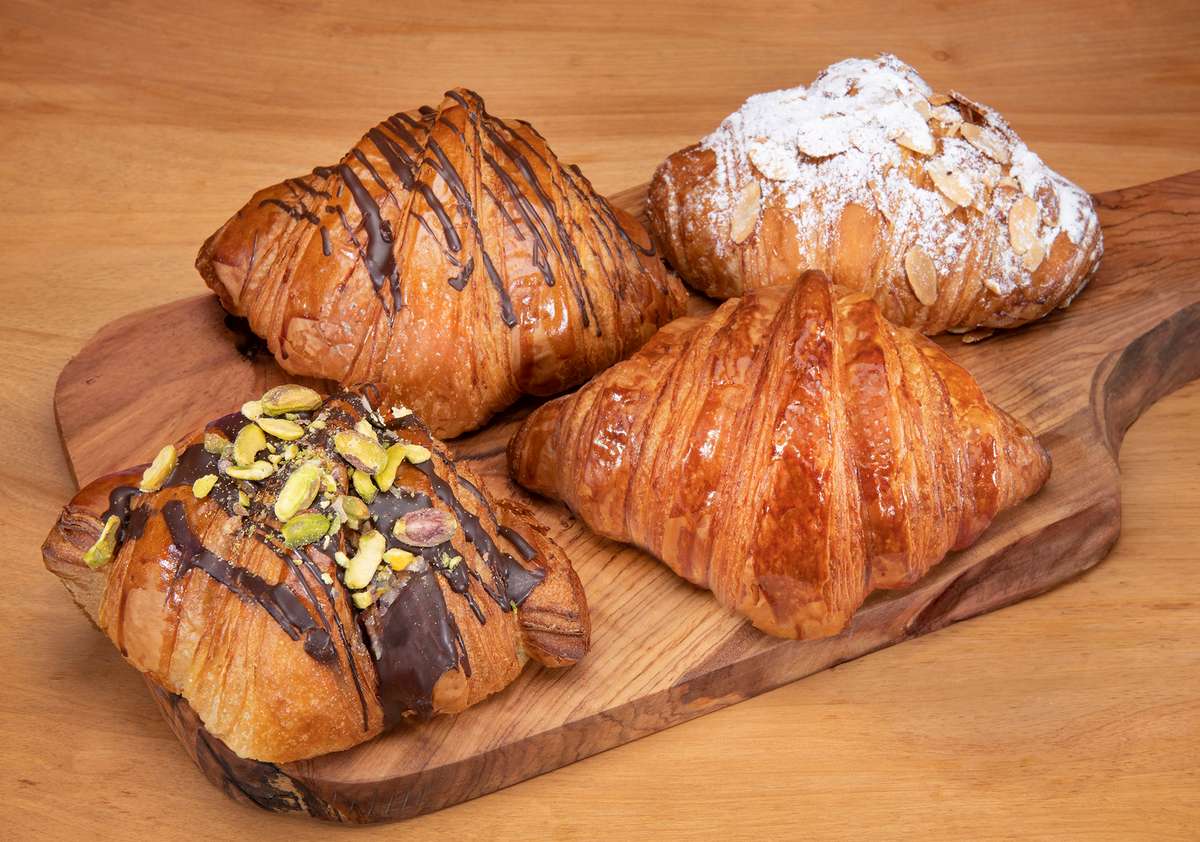 Four croissants on a wooden platter - almond chocolate plain and chocolate pistachio