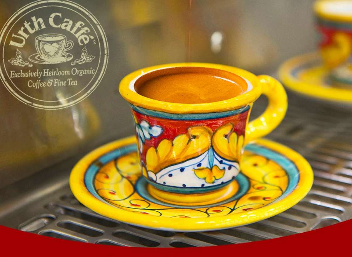 Colorful ceramic painted espresso cup and saucer with dark brown espresso dripping into a full cup.