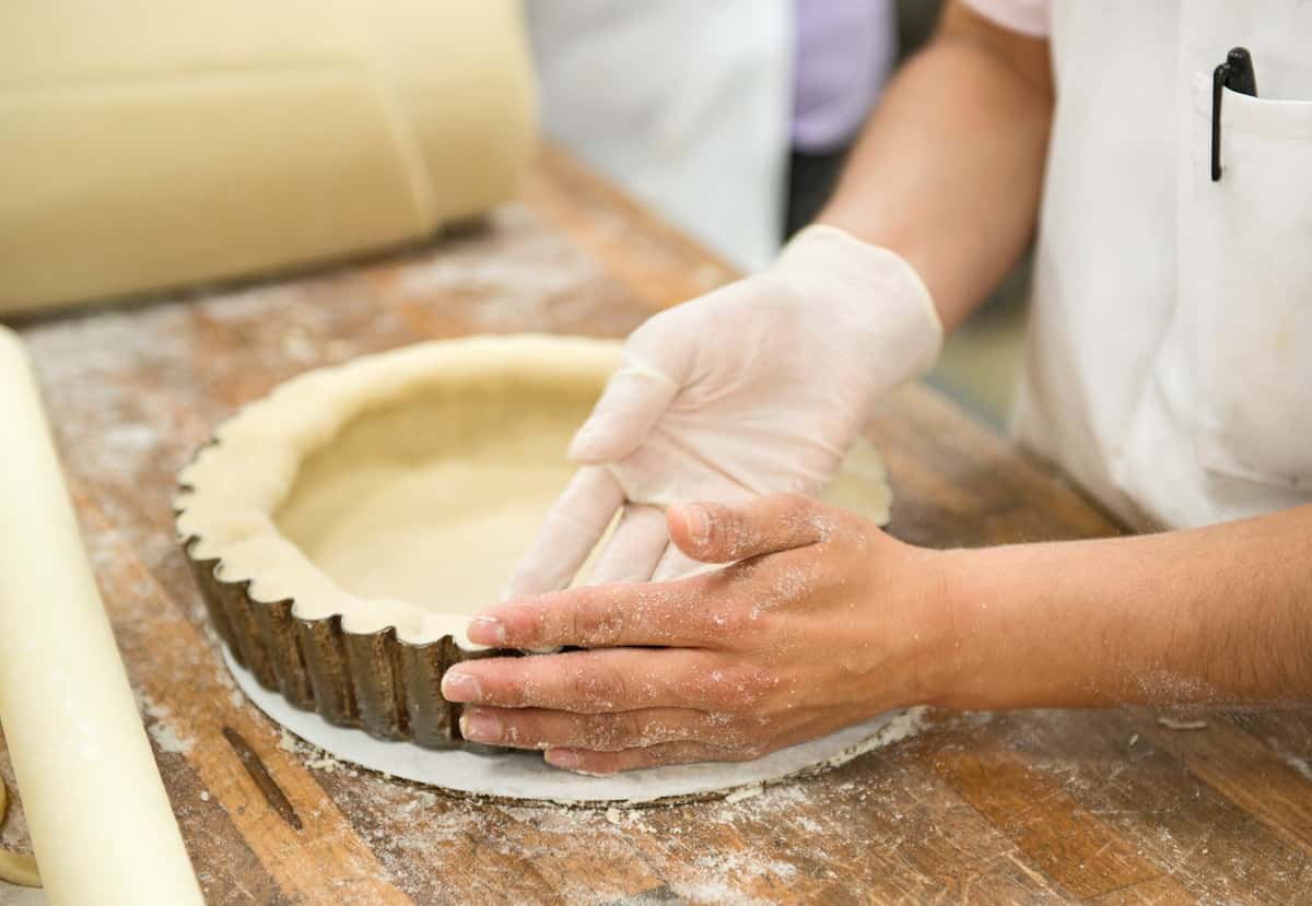 Bakery worker presses pie dough into a fluted pie pan.