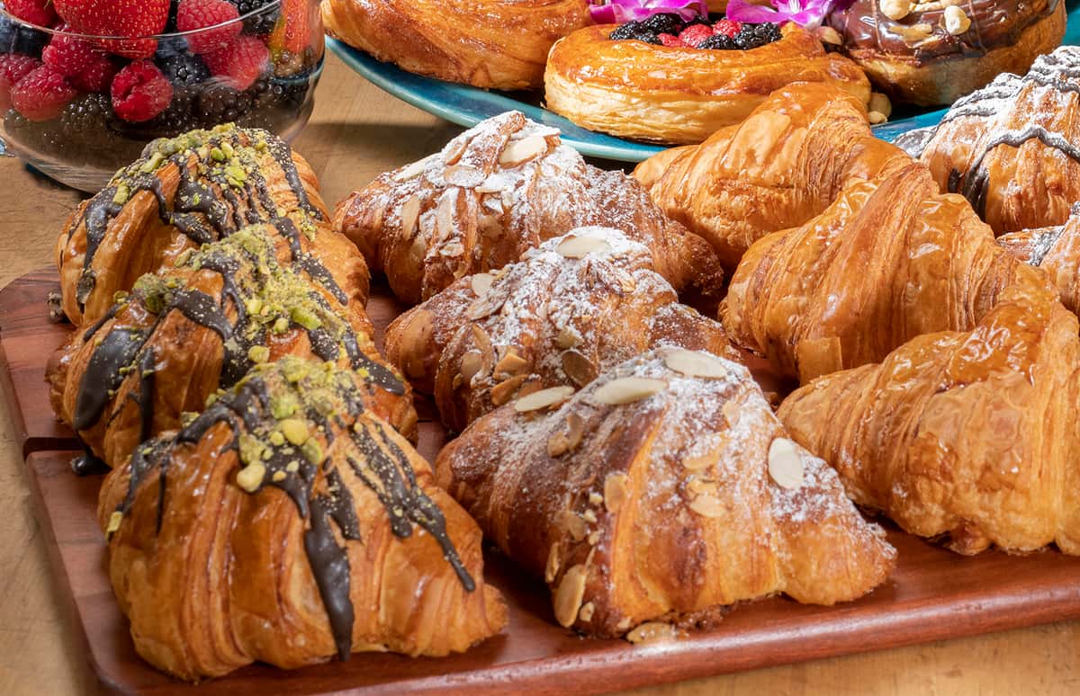 Wood platter with rows of Urth's Chocolate Pistachio, Almond and Butter croissants.