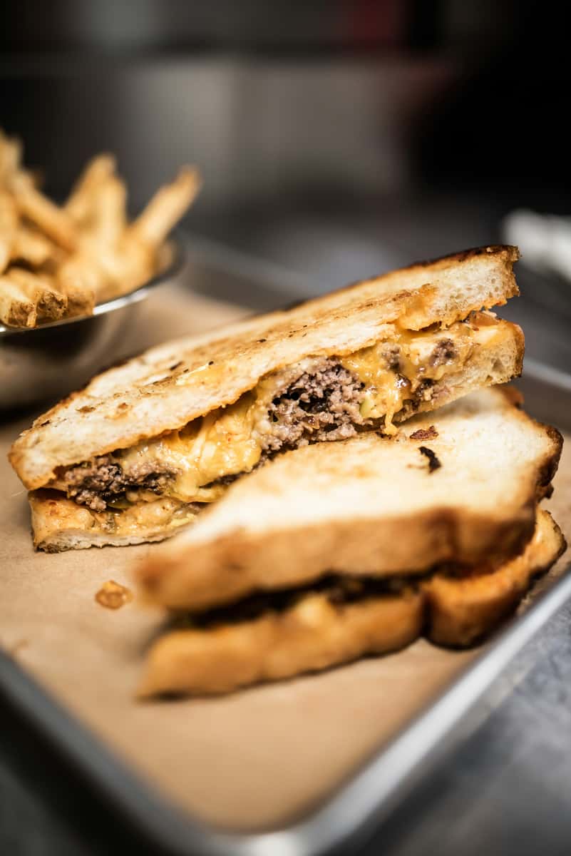 Melted cheeseburger patty melt served on grilled sourdough bread, packed with juicy ground beef and gooey cheddar cheese — a comforting American diner classic with crispy fries on the side.