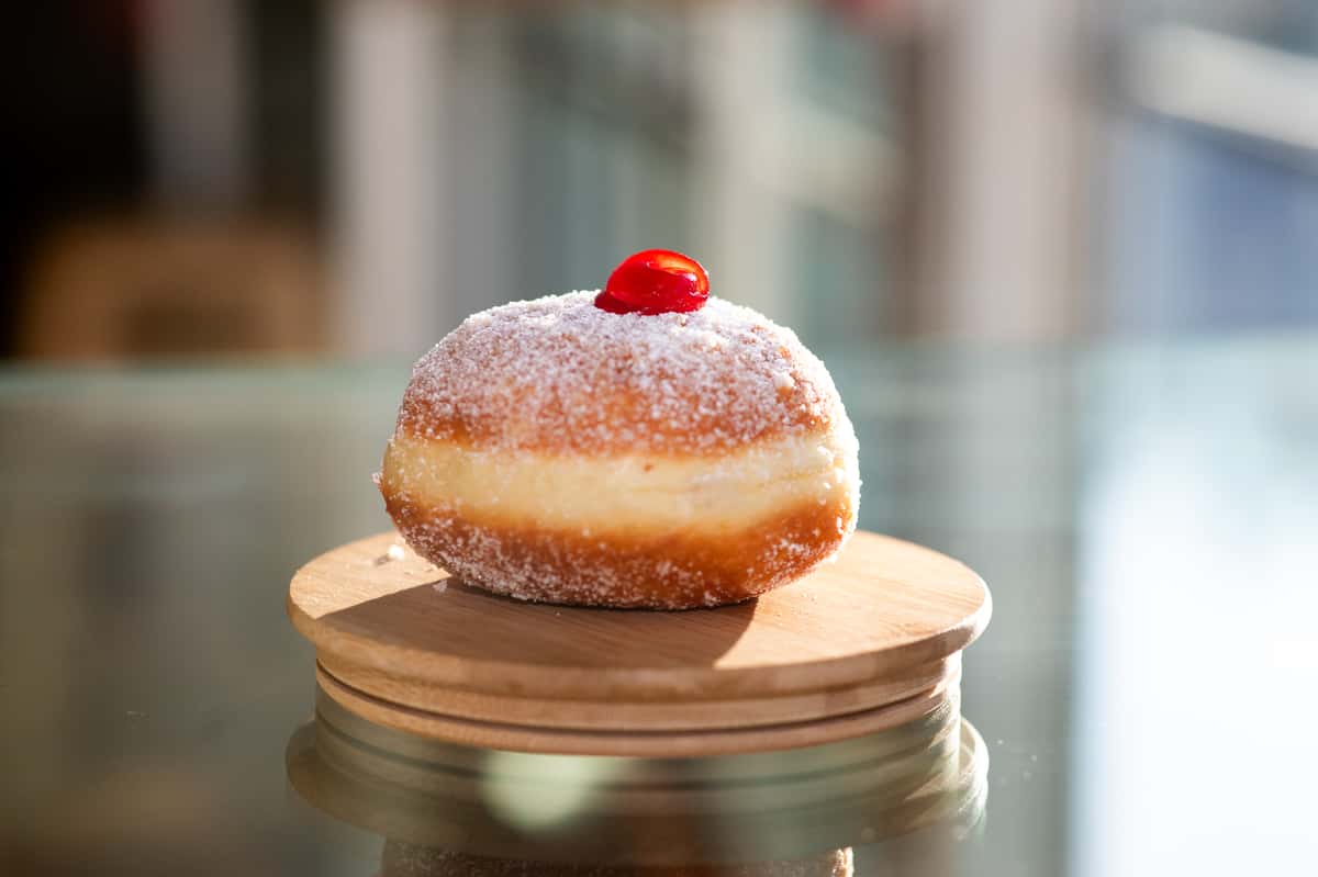Sugar-dusted bombolone topped with a red cherry on a round wooden stand at Giulia Bakery.