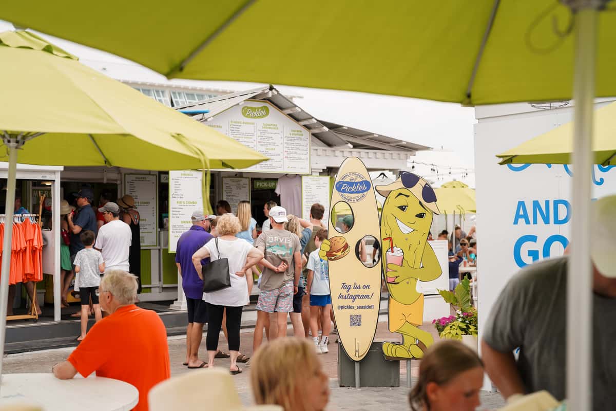 Guests gathering outside a vibrant beachfront restaurant during a busy day by the shore.