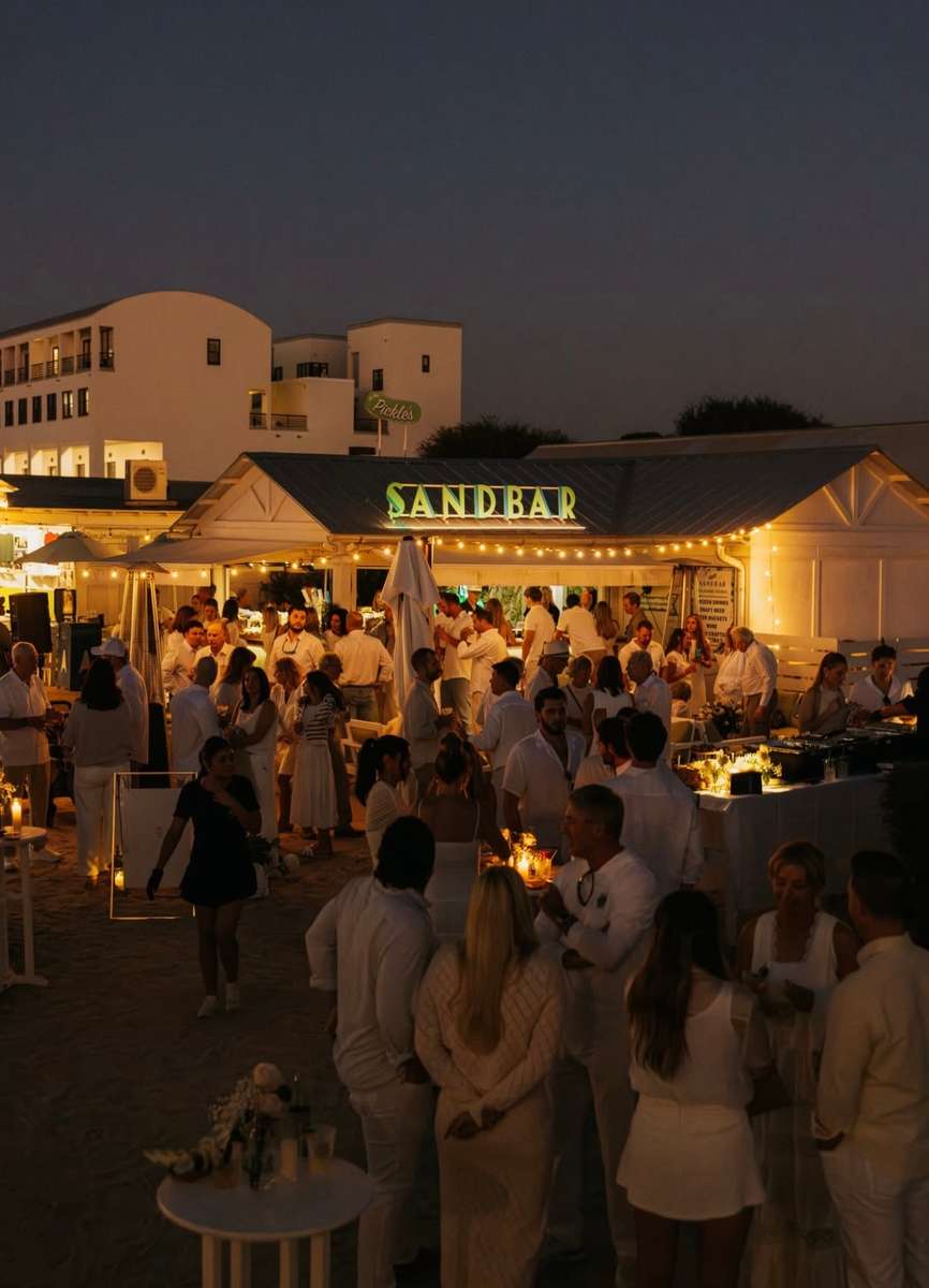 Crowd gathered for an evening event at a lively beachfront restaurant and outdoor bar.