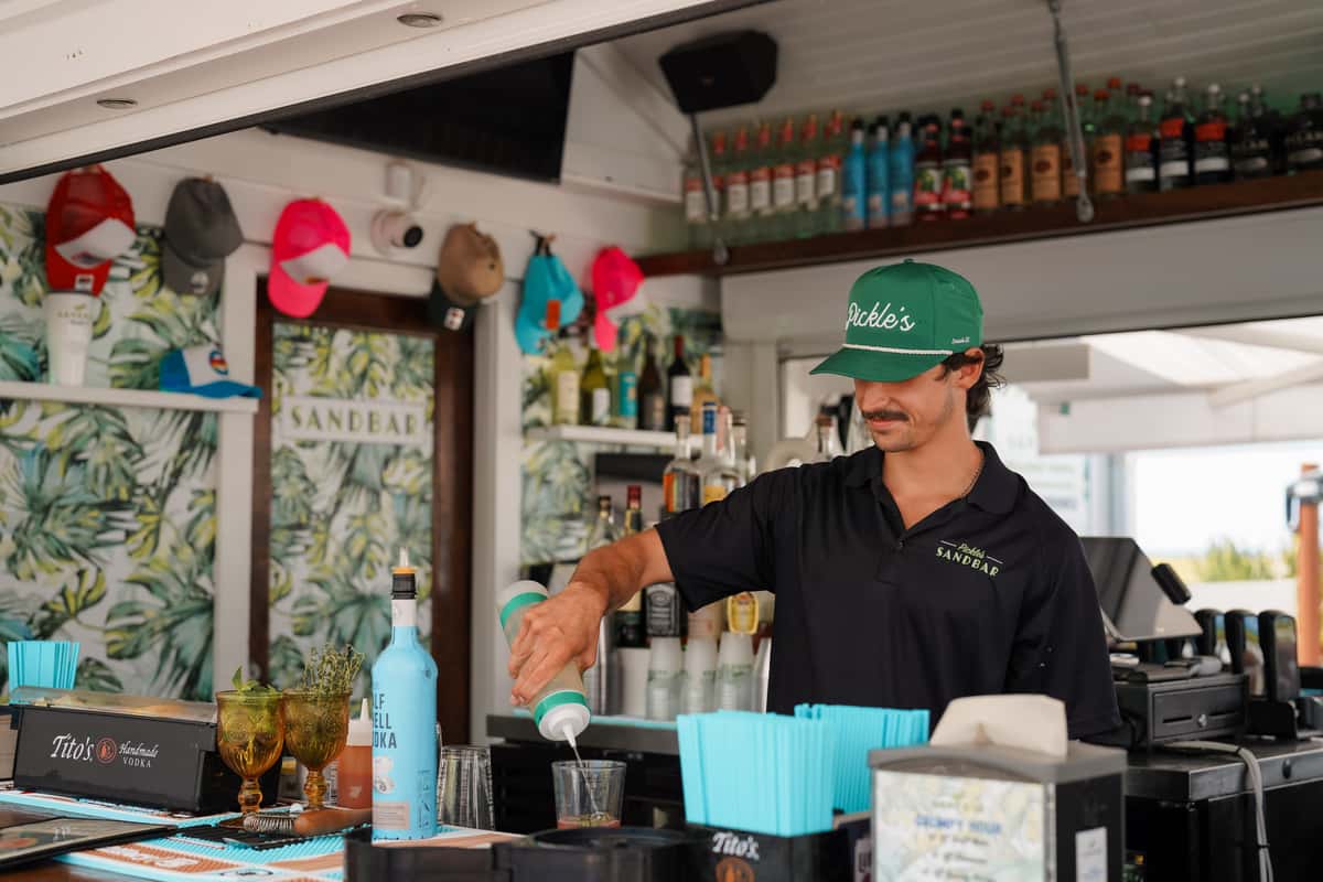 Bartender preparing drinks behind a beach bar, showcasing handcrafted cocktails and waterfront hospitality.