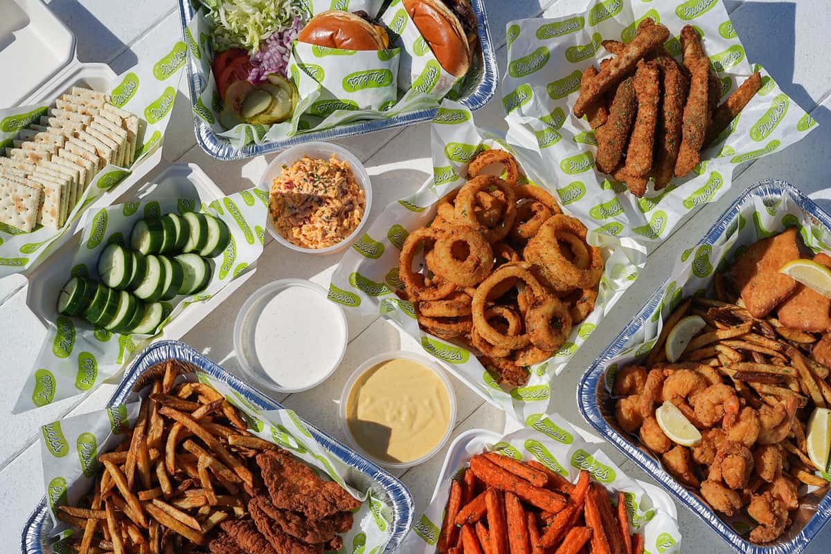 Outdoor seafood feast featuring fried shrimp, onion rings, sandwiches, sauces, and fresh sides at a coastal restaurant.