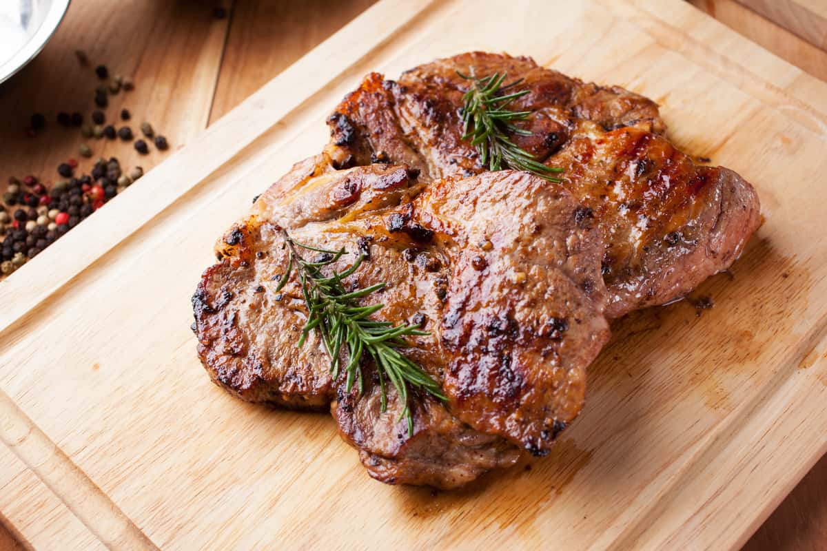 two grilled pork chops on wooden cutting board